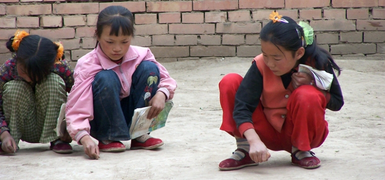 Doing homework - paper being an unneeded expense, girls practice their Chinese characters in the dirt.